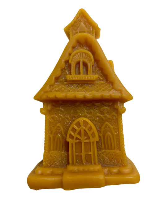 Pure beeswax candle shaped like a detailed gingerbread house, featuring an arched door, ornate windows, and a textured roof, handcrafted for holiday decor or gifting.